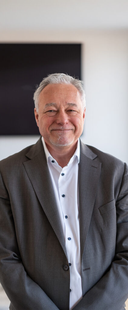 Porträt eines lächelnden Mitarbeiters der Kanzlei Seidel Runtemund + Partner in Businesskleidung vor neutralem Hintergrund.